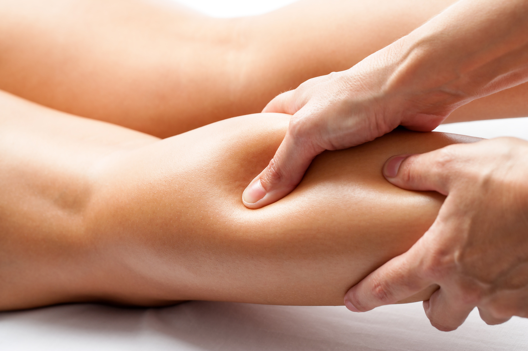 Extreme close up of osteopath applying pressure with thumb on female calf muscle.